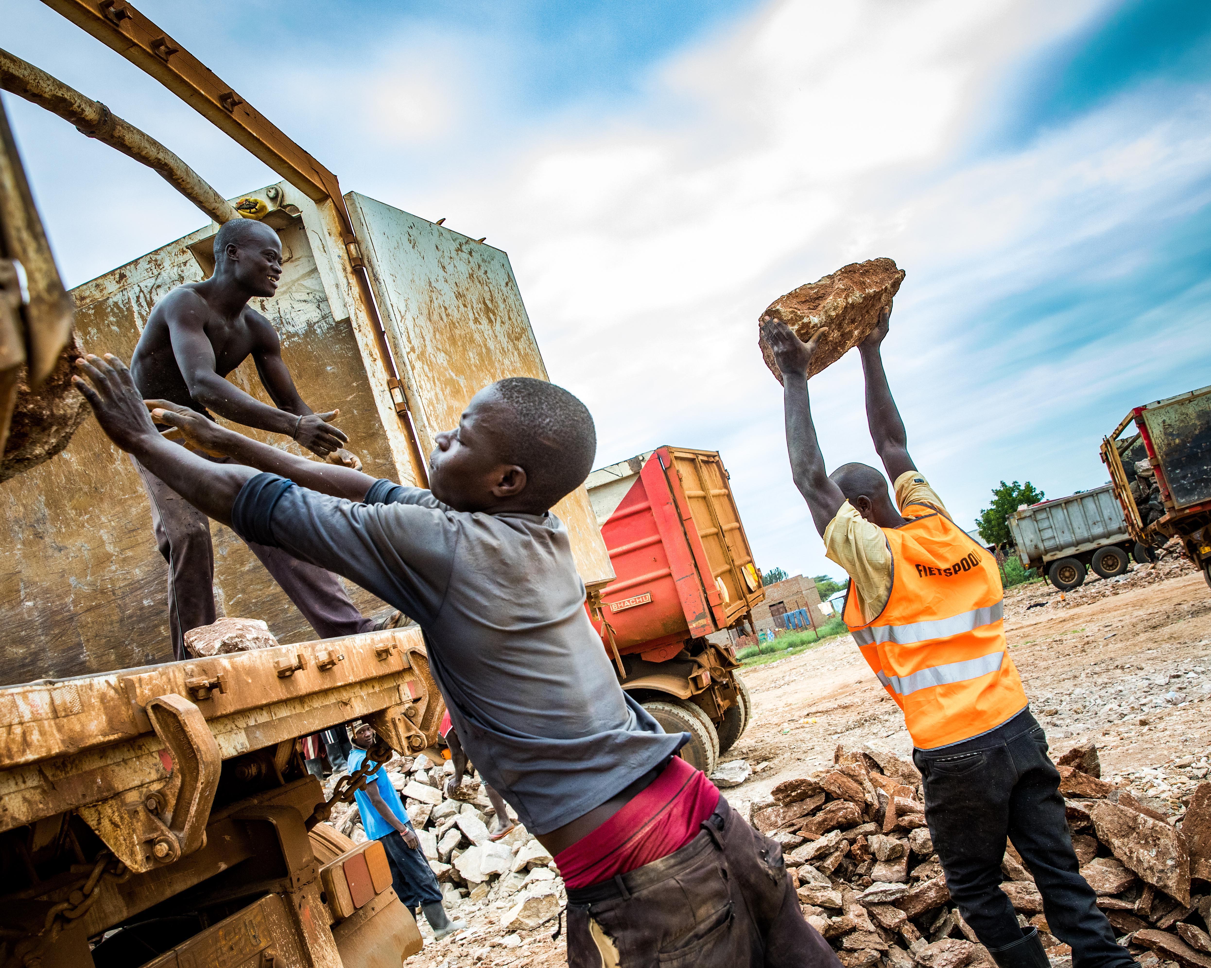 Stein für Stein verladen junge Männer den abgebauten Kalkfelsen zum Abtransport auf Lkw. 