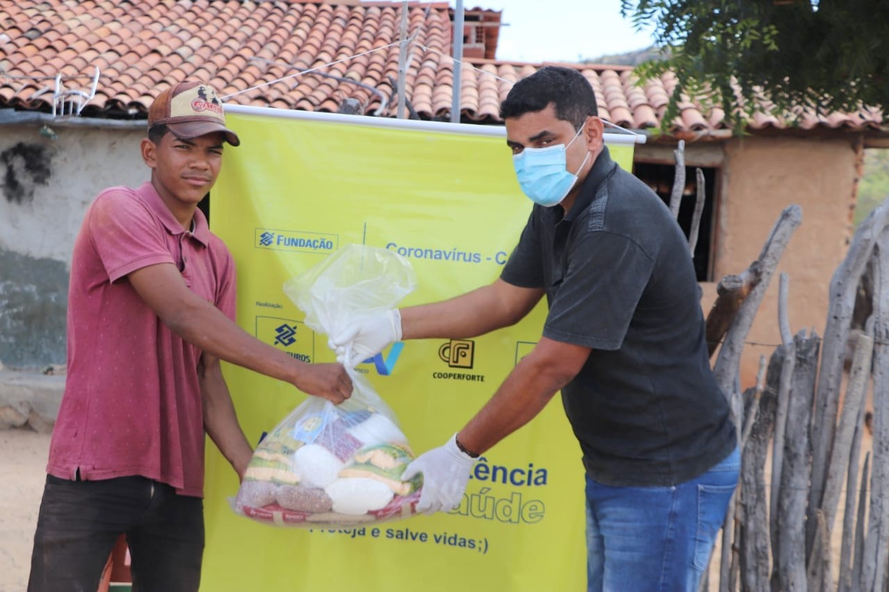 Ein Irpaa-Mitarbeiter (r.) überreicht einem Jugendlichen der Landgemeinde Olho D'Aguinha im Landkreis Sento Sé  Nahrungsmittel. Im Hintergrund das Banner der Brasilbank.