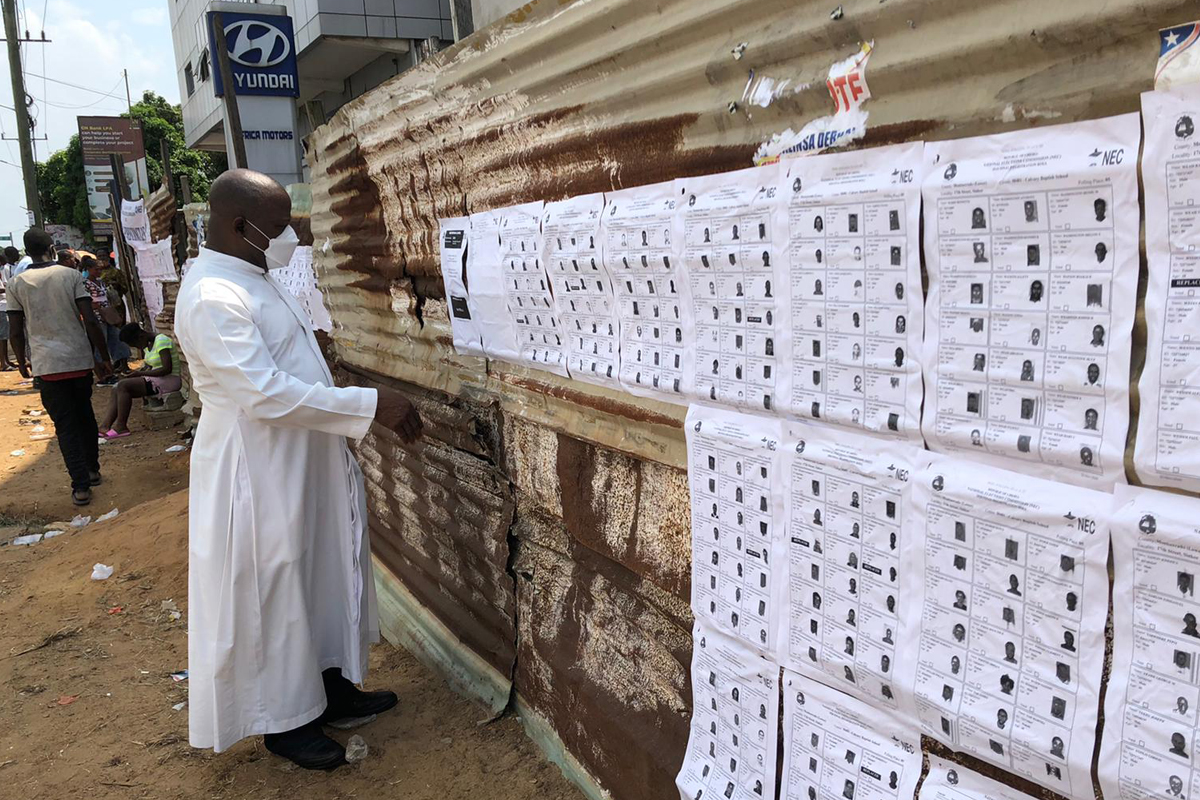 Reverend Molubah informiert sich an dieser Wahlstation über die wahlberechtigten Personen. An der Wand hängen Kopien der Wahlausweise für die Senatswahl 2020.