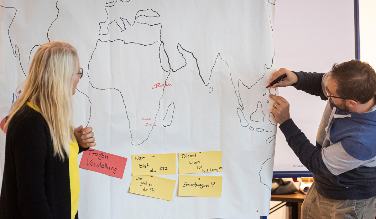 Nicola Maier, ehemalige Fachkraft, und AGIAMONDO-Referent Florian Schöpperle, zeichnen eine Weltkarte, auf der sich jede*r verorten und Gedanken oder Wünsche festhalten kann.
