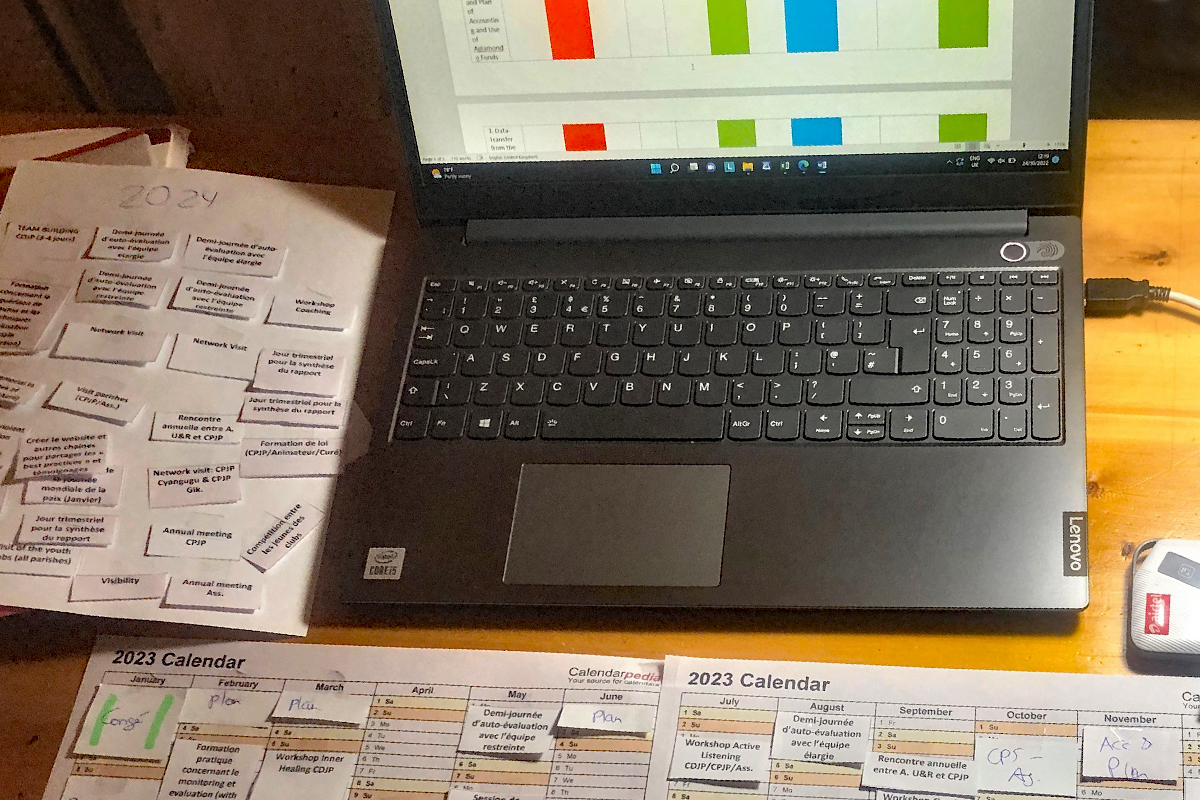 Anna-Lena Bissinger beteiligt sich mit Planungsvorlagen auf dem Laptop und analogen Übersichten an den Projektplanungen der CDJP Gikongoro in Nyamagabe für 2023.