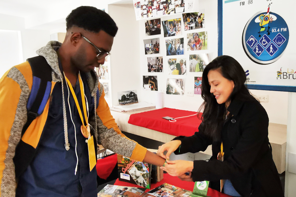 Jhon Alexis Viveros Valencia (links) besucht den Stand der Organisation Compromiso und bekommt dort von Angélica María Rivero Fuentes ein Armband von Compromiso geschenkt.