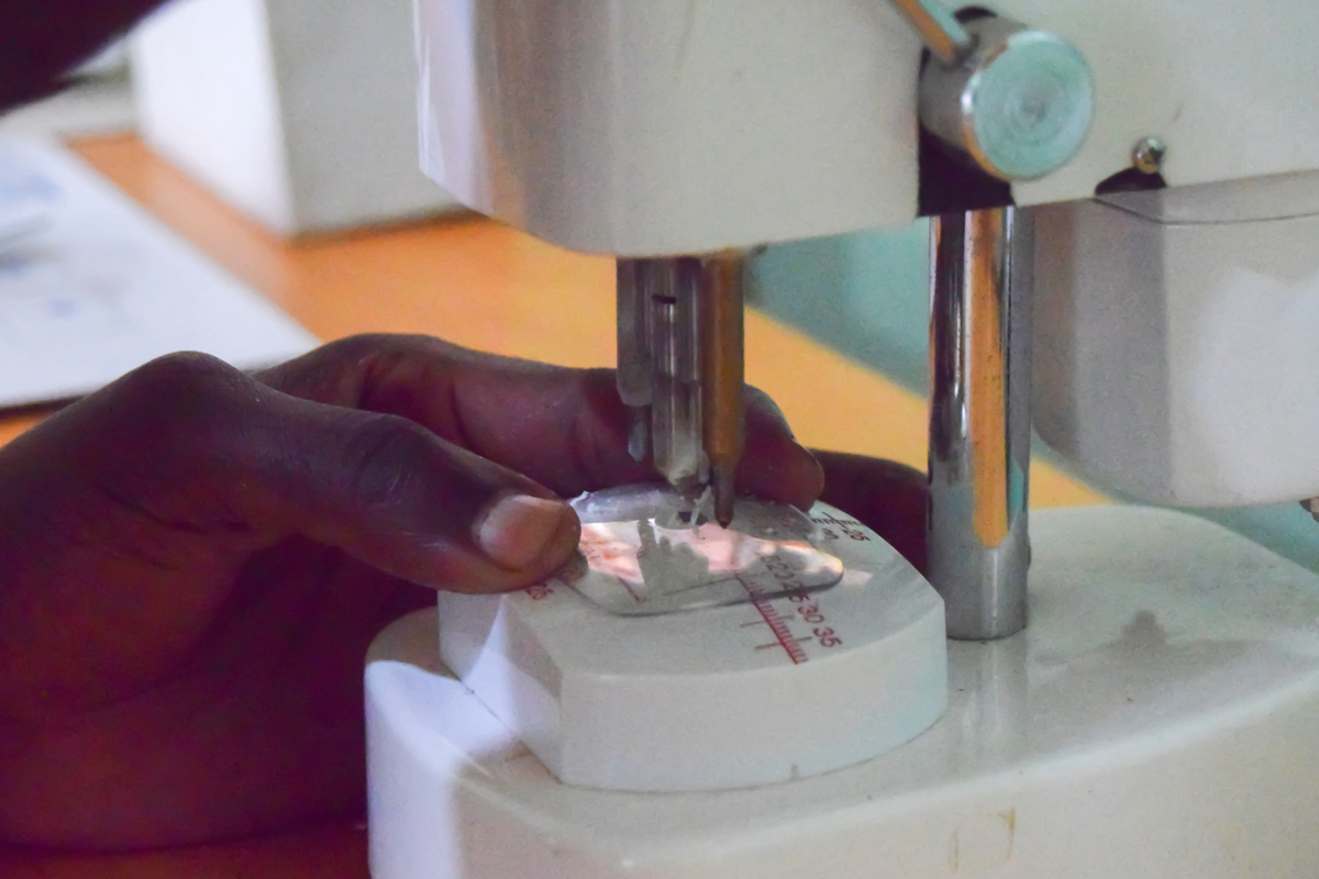 Ein Auszubildender bereitet eine Formscheibe mit der richtigen Zentrierung vor. Mehrere kleinteilige Arbeitsschritte sind notwendig, bis eine Brille fertiggestellt ist.