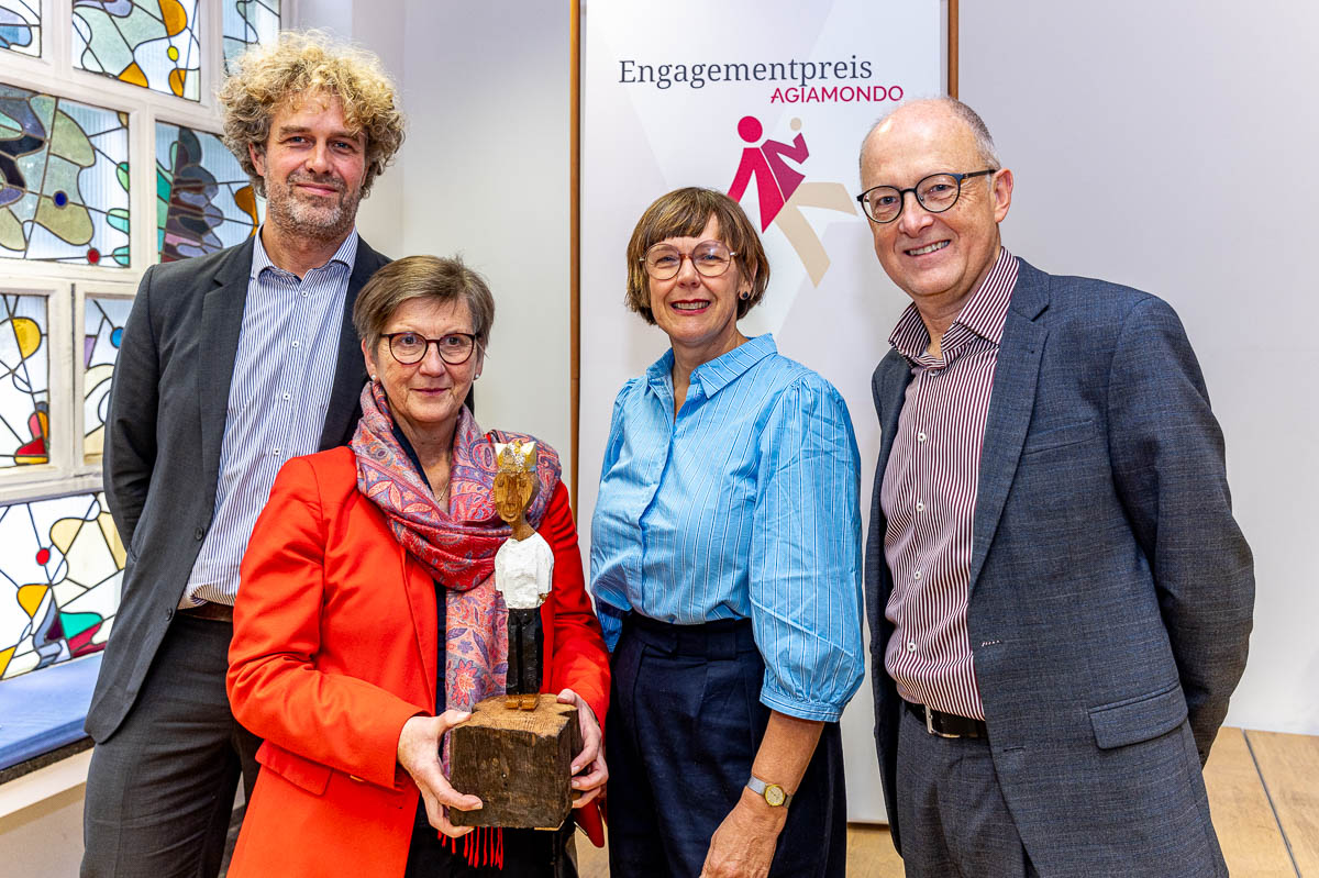 2 Männer und 2 Frauen stehen in einer Reihe mit einer Skulptur