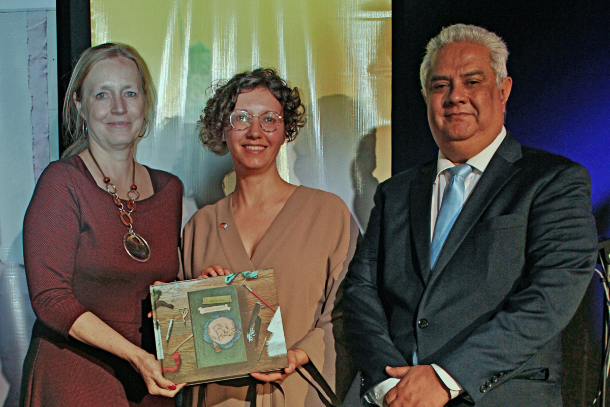 Buchvorstellung vor Publikum Drei Personen halten das Buch der Erinnerung hoch und zeigen es dem Publikum.